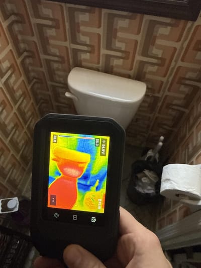Infrared camera image of the toilet, the cool blue area on the wall behind it showing moisture evaporating