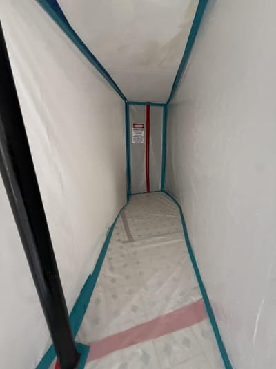 A hallway fully sealed in plastic containment with a Danger Asbestos warning sign posted inside