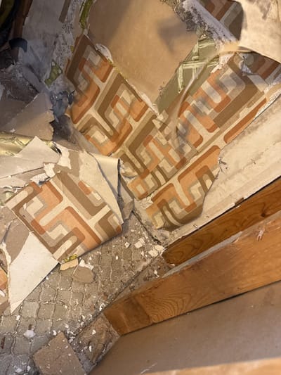 Wallpaper peeled back from the bathroom drywall, showing the moisture it had been sealing in