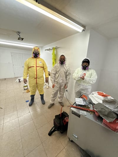 Three abatement workers in protective suits and respirators ready to begin removal in a tiled room