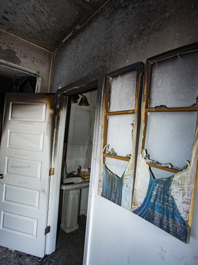 A fire-damaged room with heavy soot on the walls and ceiling and a charred, burned-out window frame