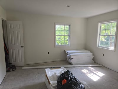 A rebuilt room with a repaired ceiling, new drywall and fresh paint, and boxed flooring stacked on the bare subfloor ready to install
