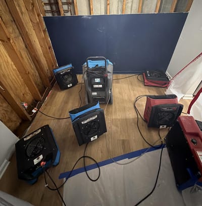 Several air movers and a dehumidifier running in a stripped room during the drying phase of a mold job