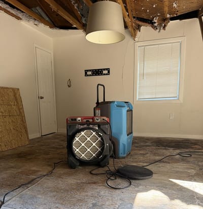 An air mover and dehumidifier drying an empty room below a collapsed, water-damaged ceiling