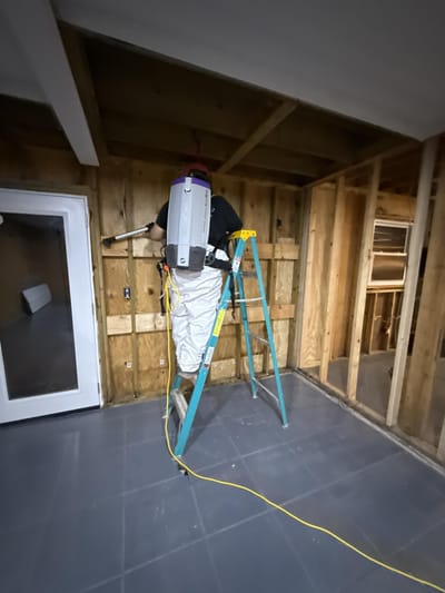 HEPA-vacuuming surfaces from a ladder during the top-down cleaning