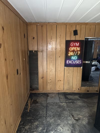Gym wall paneling removed, exposing the layered wall and fire damage in the cavity