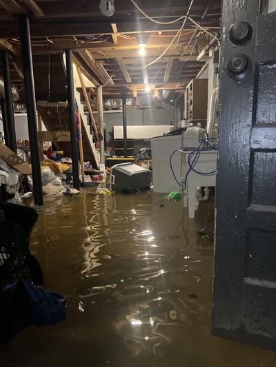 Muddy floodwater covering a basement floor around a washer, dryer and stored belongings