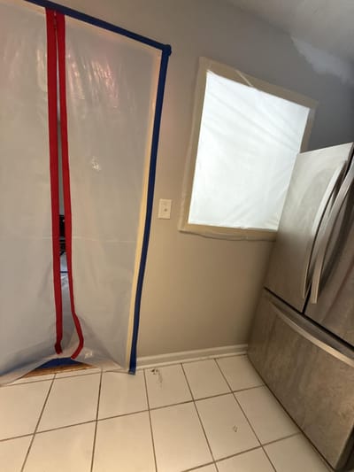 A zippered containment door across the kitchen entry, with the window sealed off in plastic