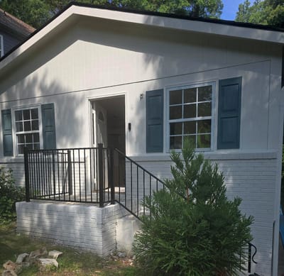 The front of a house after a rebuild, with a repaired roofline, freshly painted siding and brick, new blue shutters and a new porch railing