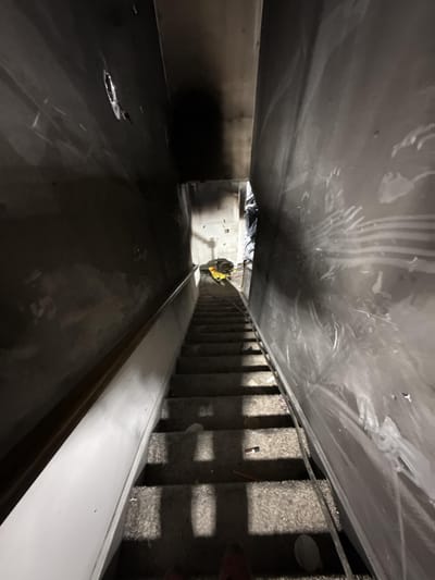 A staircase and walls coated in dark soot and smoke residue after a fire