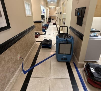 A dehumidifier and air movers running down a clean office hallway during drying