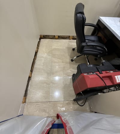 An office with the baseboards removed and an air mover drying the wall base