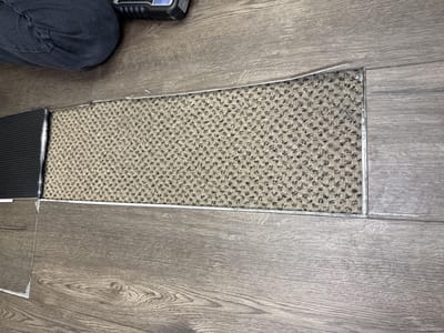 A section of vinyl plank removed, exposing the commercial carpet glued underneath